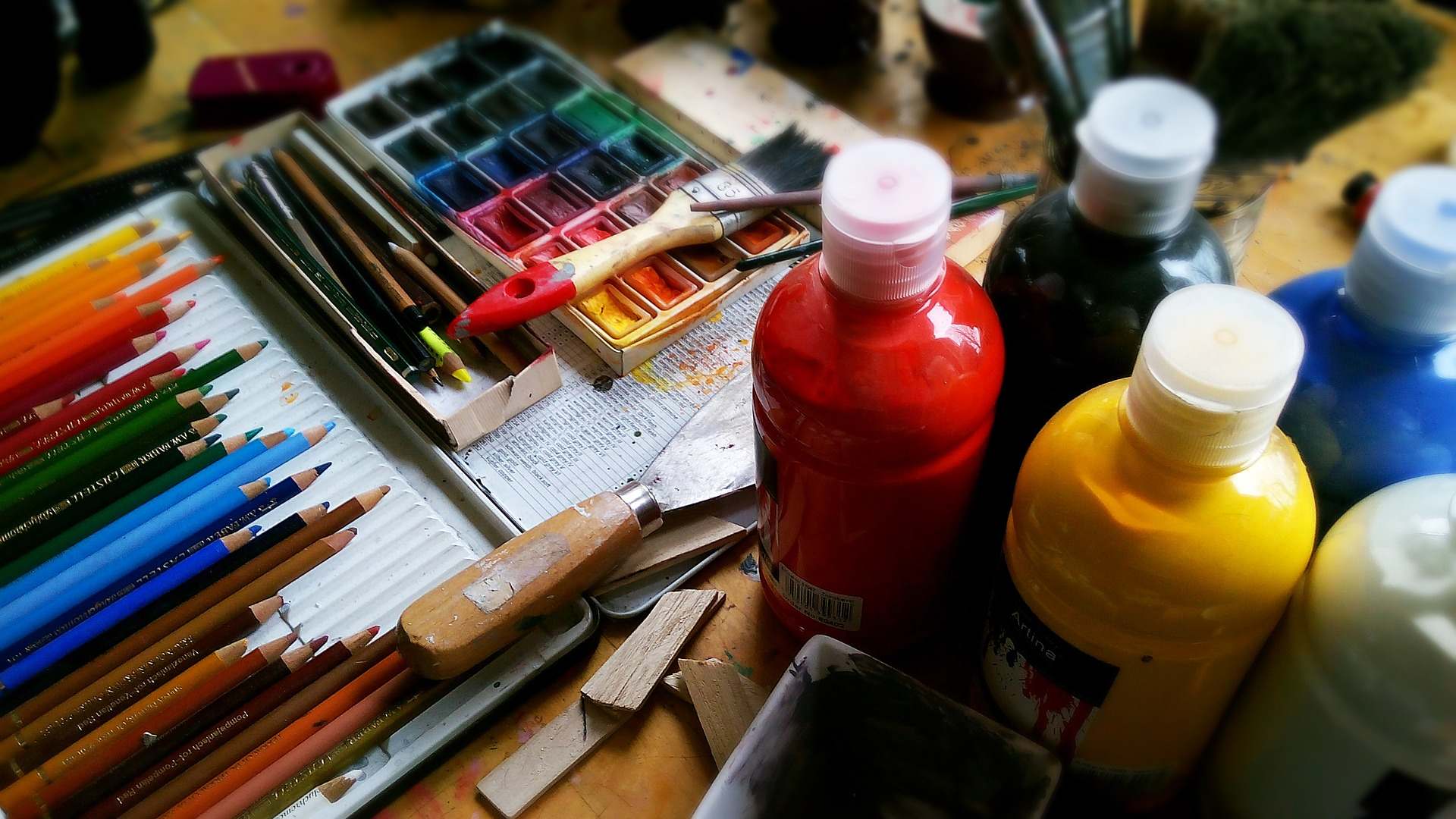 Blick auf einen Malertisch mit Wasserfarben, Farben in Flaschen, eine Spachtel und bunte Stifte